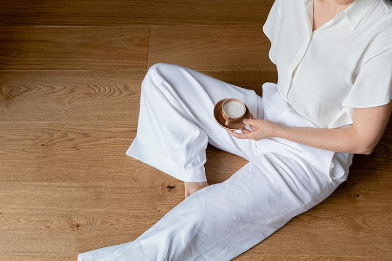 Lifestyle photo of a person dressed in all white holding a cappuccino while sitting on a hardwood floor from Couture by Kentwood.