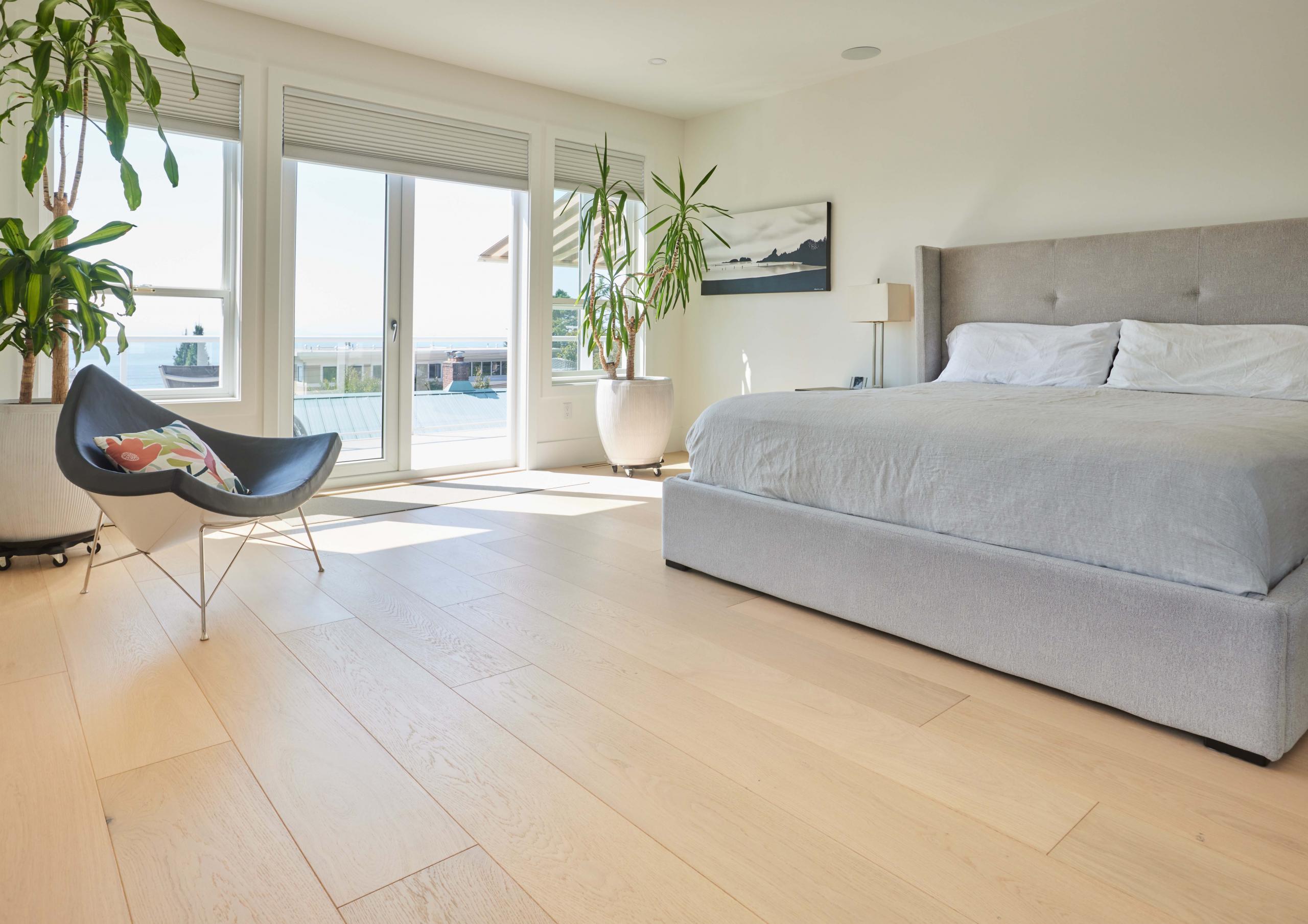 Photo of an ocean-view bedroom with minimalist interior design. There is a bed to the right of the image, and a designer chair on the left side. The Tulum floor from Couture by Kentwood is prominently featured in the photo.